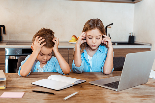 tired siblings e-learning near notebook and laptop at home