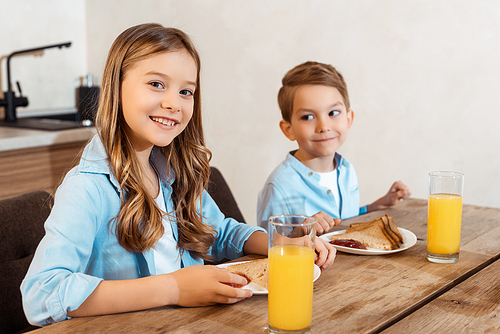 selective focus of happy kid smiling near brother and tasty breakfast