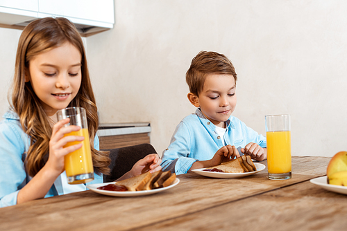 selective focus of happy sister holding glass of orange juice near brother and tasty breakfast