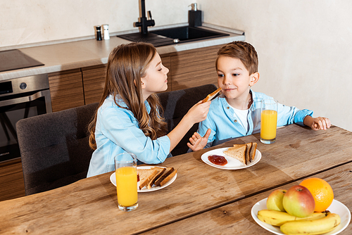 cute sister feeding brother with toast bread at home