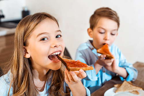 selective focus of cheerful siblings eating toast bread with bread