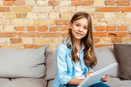 happy kid sitting on sofa and writing in notebook