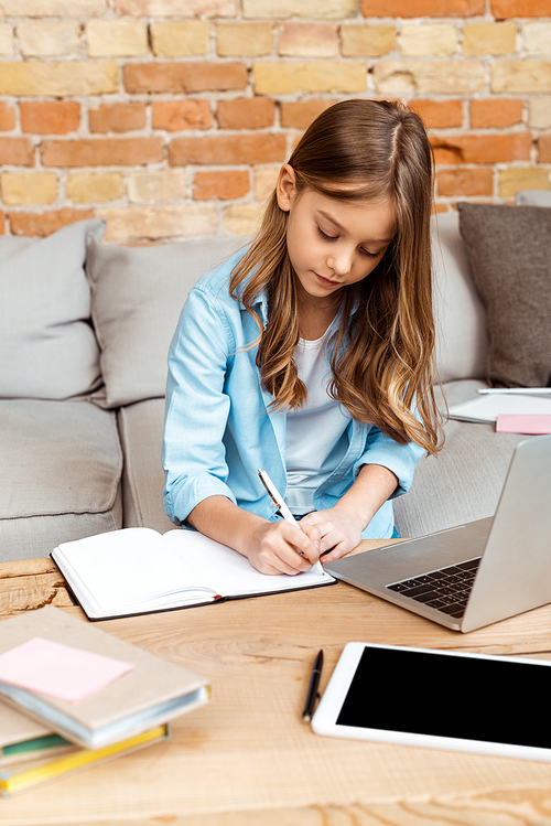 cute kid writing in notebook while e-learning at home