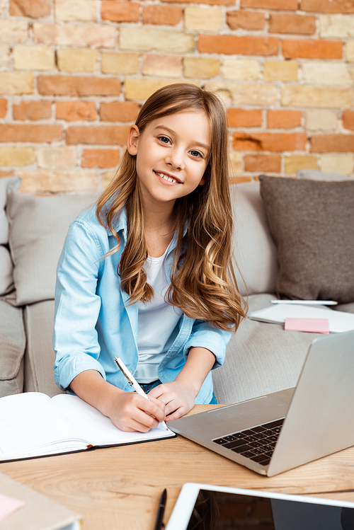 happy kid writing in notebook while e-learning at home