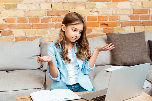 confused kid showing shrug gesture and looking at laptop