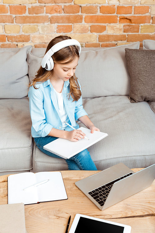 cute kid in headphones writing in notebook near gadgets