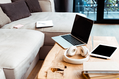 selective focus of gadgets with blank screen near wireless headphones on coffee table