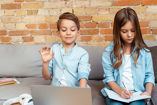 cute boy waving hand while having video call near sister in living room