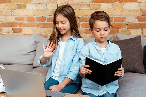 cute kid waving hand while having video call near brother in living room