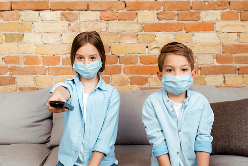 selective focus of siblings in medical masks watching movie at home