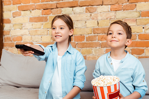 selective focus of kid holding remote controller near brother with popcorn bucket