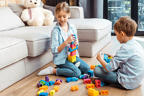 cute siblings playing with building blocks while sitting on floor in living room