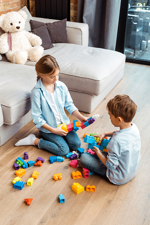 siblings playing with building blocks while sitting on floor in living room