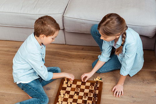 overhead view of siblings playing chess on floor in living room