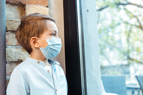 boy in medical mask looking at window