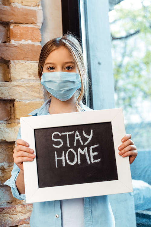 kid in medical mask  and holding chalkboard with stay home lettering