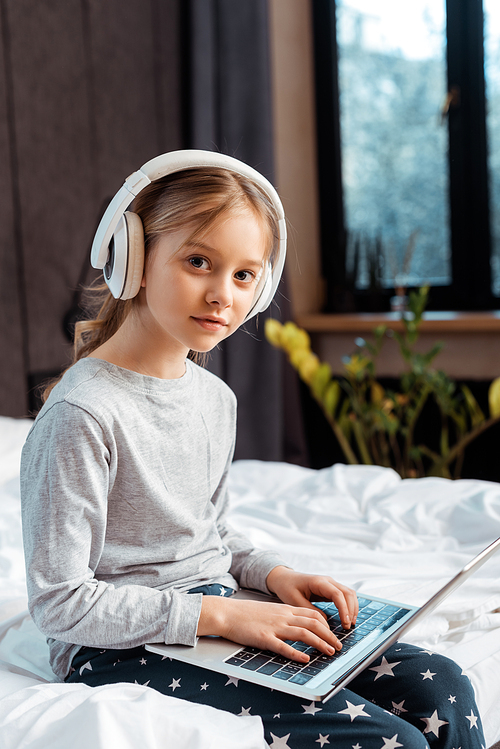 child in wireless headphones using laptop with e-learning in bedroom