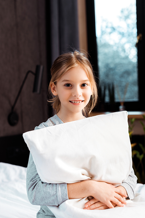 cheerful kid smiling while holding pillow in bedroom