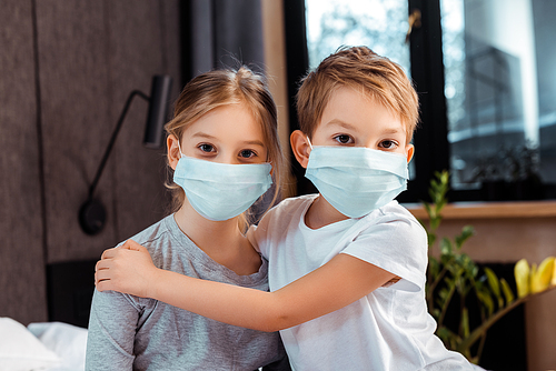 cute brother hugging sister in medical mask at home