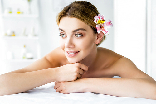 attractive and smiling woman with flower lying on massage mat