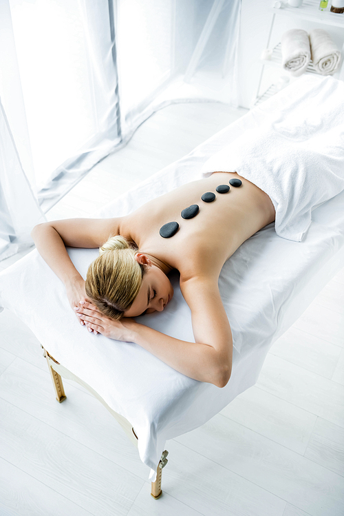 high angle view of attractive woman with hot stones on back lying on massage mat