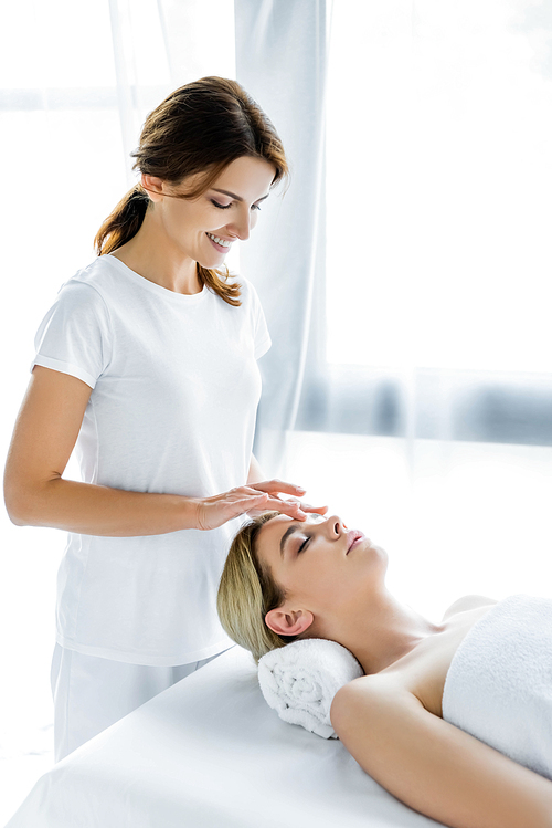 smiling masseur doing face massage to attractive woman in spa