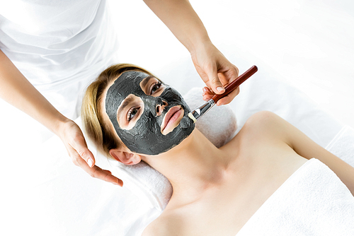 cropped view of beautician applying clay mask on face of woman