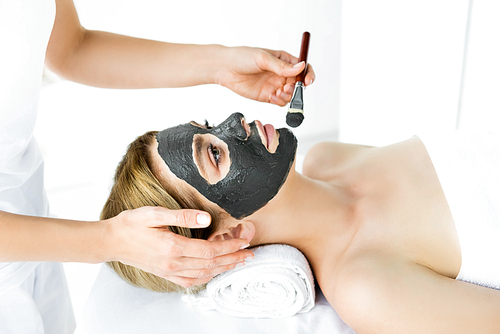 cropped view of beautician applying clay mask on face of woman