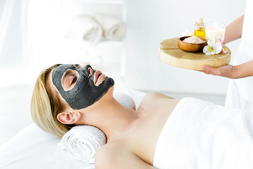 attractive woman with clay mask on face lying in spa