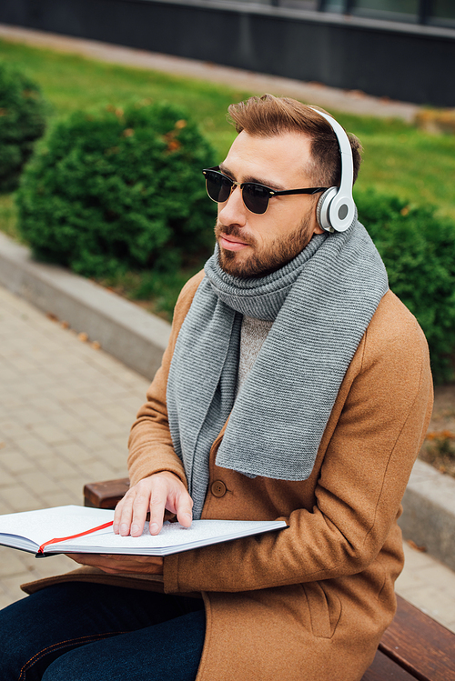 Blind man in headphones reading book with braille font in park
