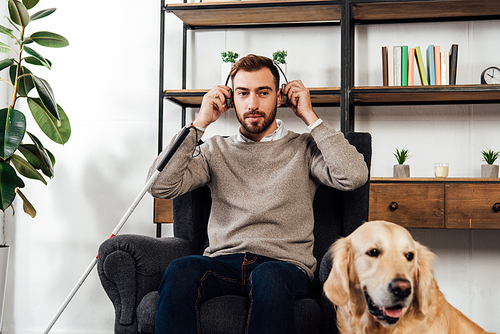Visually impaired man using headphones beside golden retriever at home