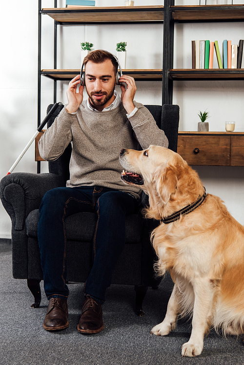 Blind man listening music with headphones beside golden retriever at home