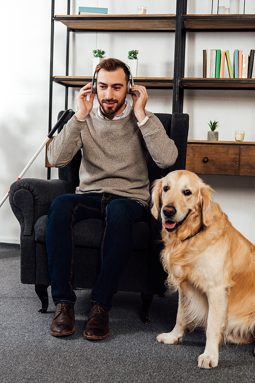 Visually impaired man listening music with headphones beside golden retriever at home