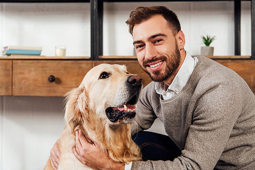 Smiling man  while petting golden retriever at home