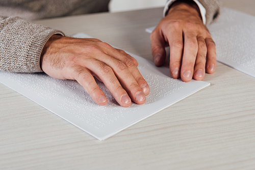 Cropped view of bind man reading braille font on paper at table
