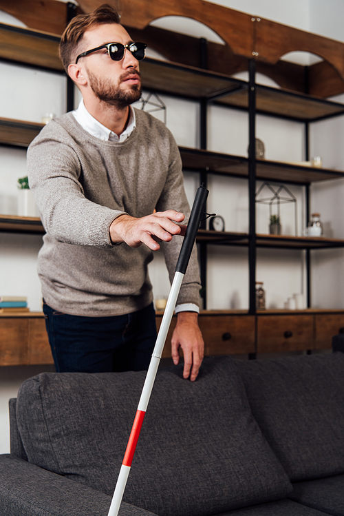 Blind man pulling hand to walking stick in living room