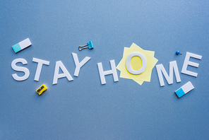 Top view of stay home lettering near stationery on blue surface