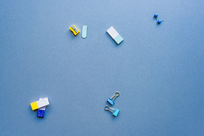Top view of pencil sharpener, binder clips and erasers on blue background