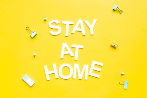 Top view of stay at home lettering near binder clips and pencil sharpener on yellow surface