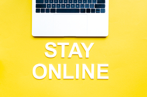 Top view of stay online lettering and laptop on yellow surface