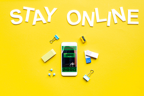 Top view of stay online lettering near smartphone with booking app on yellow surface