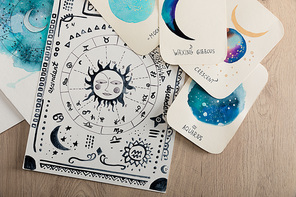 Top view of birth chart and cards with zodiac signs on wooden table