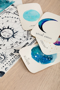 Cards with watercolor drawings of moon phases and birth cart with zodiac signs on table