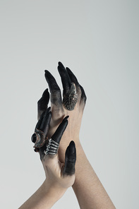 Cropped view of witch hands with black dye and jewelry rings isolated on grey