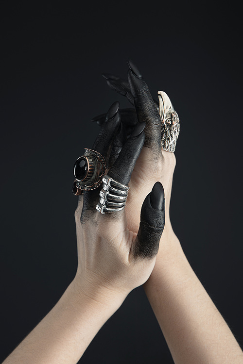 Cropped view of hands of witch with jewelry rings and black dye isolated on black