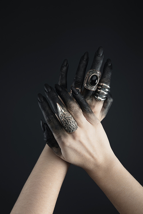Cropped view of black painted hands of witch with jewelry rings isolated on black