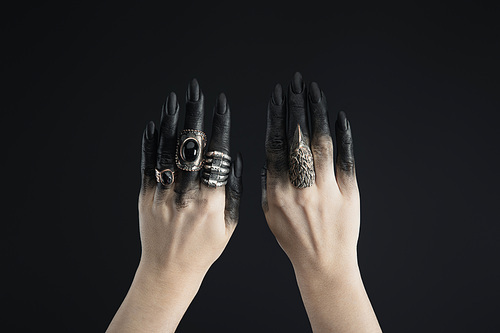 Cropped view of black painted hands of witch with jewelry rings isolated on black