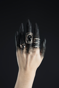 Cropped view of jewelry rings on black painted hand of witch isolated on black