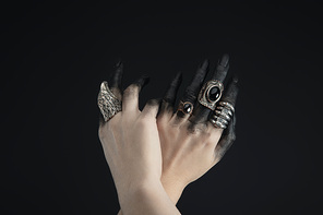 Cropped view of witch hands with jewelry rings and black paint isolated on black