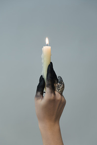 Cropped view of witch with black dye on hand holding candle isolated on grey